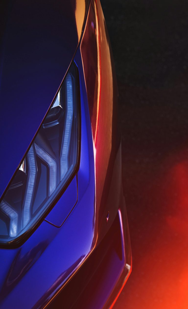 Vibrant close-up of a luxury sports car headlight featuring lens flare and reflections.